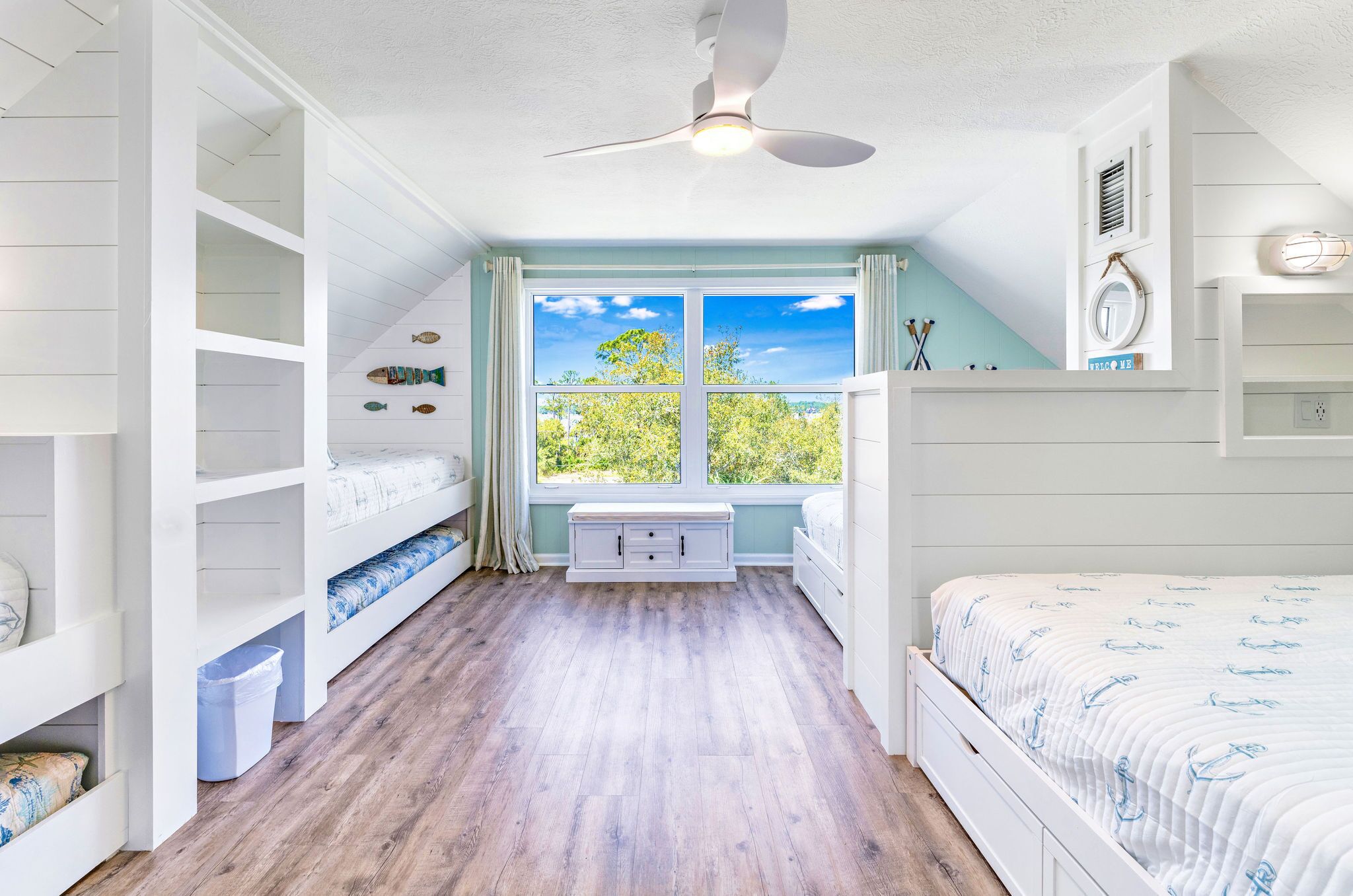 A bedroom with a large window, built-in shelving, a ceiling fan, and a bed with a patterned bedspread.
