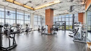 Un gimnasio amplio con diverso equipo de ejercicio, ventanas grandes y un techo alto.