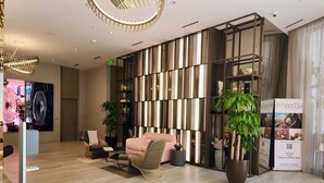 Un lobby moderno con piso de madera, un sofá rosa, una silla de mimbre y una planta grande en maceta.