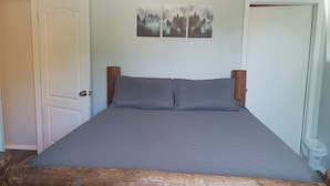 Una cama con cabecera de madera, colchón gris y una obra de arte en la pared con motivos de árboles.