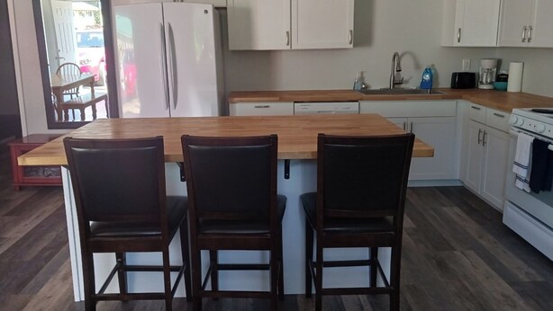 Una cocina moderna con armarios blancos, encimera de madera y una isla central con tres sillas.