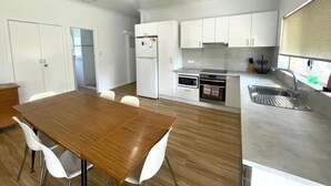 A modern kitchen with white cabinets, a wooden dining table, and a stainless steel sink. - The EOS 2, Esperance (Esperance)
