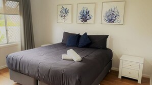 A bedroom with a large bed, a white nightstand, and three framed wall art pieces. - Blue Tides Holiday Accommodation (Castletown)