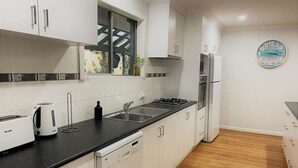 A modern kitchen with white cabinets, a black countertop, a Breville toaster, a kettle, a sink, a stove, and a refrigerator. - Blue Tides Holiday Accommodation (Castletown)
