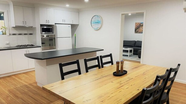 A modern kitchen with white cabinets, a wooden dining table, and a black countertop. - Blue Tides Holiday Accommodation (Castletown)