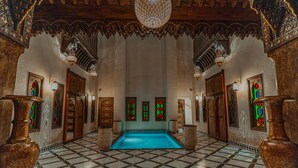 Un amplio pasillo con suelo de tablero de ajedrez, arcos ornamentales y una piscina central.