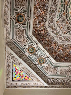A detailed ceiling with geometric patterns and a stained glass window. - Riad Deluxe (Marrakech)