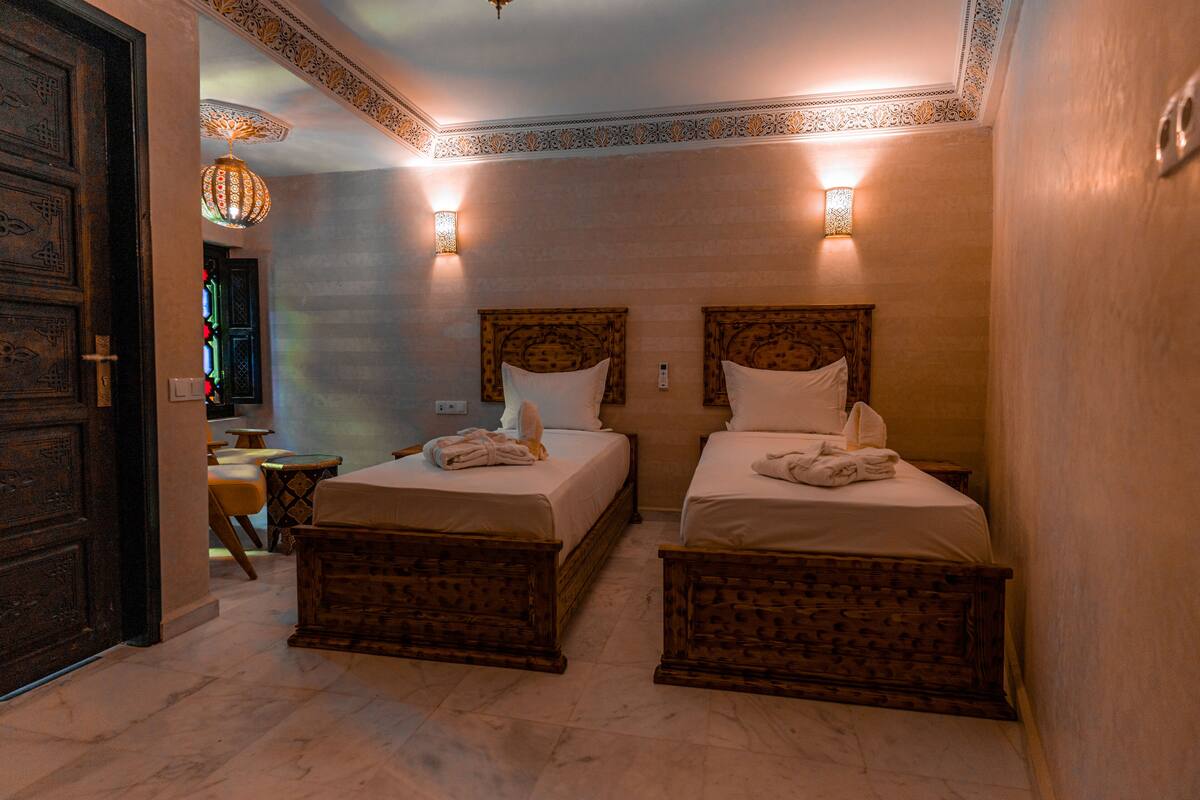 A hotel room with two wooden beds, a small table, and a decorative ceiling light.