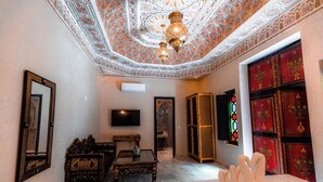 Una habitación con una cama, televisor, espejo, mesa y un techo decorativo.