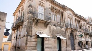 Un edificio histórico con arquitectura clásica, que presenta un balcón, arcos en las puertas y una fachada orientada a la calle.