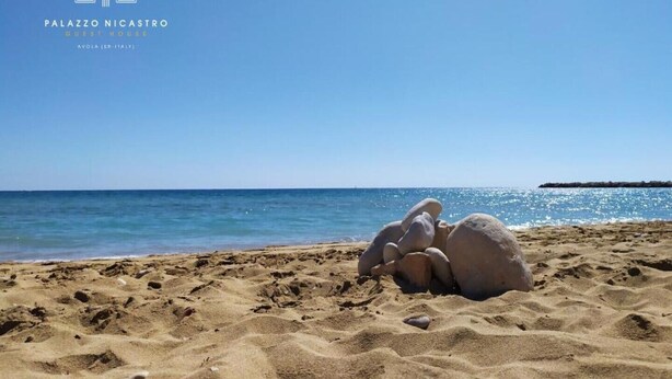 Una playa con arena y rocas, cielo despejado y mar tranquilo.