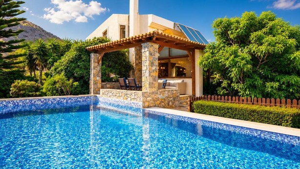 Una piscina con borde de piedra y azulejos, un área de estar cubierta con sillas, y una montaña al fondo.