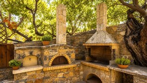 Cocina exterior de piedra con horno de pizza, horno de ladrillo y chimenea.