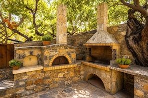 Cocina exterior de piedra con horno de pizza, horno de ladrillo y chimenea.