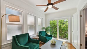 Una habitación con dos sillones verdes, una mesa de centro de madera, una lámpara de pie y un ventilador de techo.