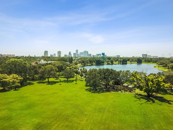 A park with a lake, trees, and a city skyline in the background.