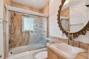 A bathroom with a glass-enclosed shower, a white bathtub, a sink with a marble countertop, and a large ornate mirror.