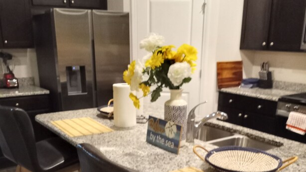 A modern kitchen with granite countertops, stainless steel appliances, and black chairs.