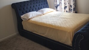 A bedroom with a tufted headboard, a bed with a patterned bedspread, a ceiling fan, and floral curtains.