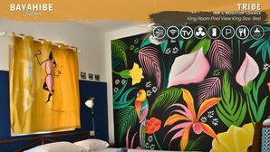 A room with a bed, a yellow curtain with a cartoon character, a vibrant floral mural, and a wooden chair. - Tribe Inn & Rooftop Lounge (San Rafael del Yuma)