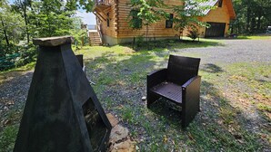 Una cabaña de troncos con chimenea de piedra, un sillón de mimbre y una terraza de madera.