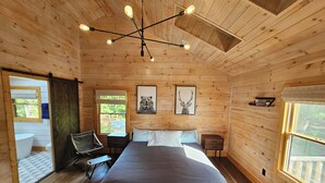 Un dormitorio de cabaña de madera con una cama, dos mesitas de noche, una silla y una ventana.