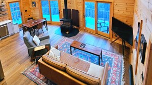 Una cabaña espaciosa con techo alto, paredes de madera, chimenea, comedor y ventanas amplias con vistas al exterior.