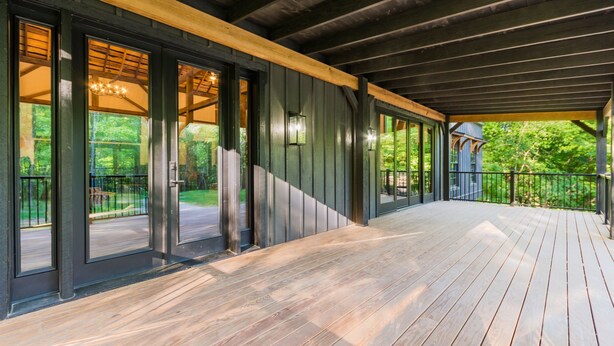 Une terrasse en bois couverte, avec des portes vitrées donnant sur un espace patio.