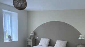A bedroom with a large bed, two bedside tables, a window with curtains, and a hanging light fixture. - Ferme Familiale Rénovée Dans un Village Tranquille (La Vendeix, GELLES)