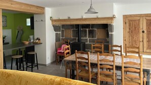 A dining area with a stone fireplace, wooden chairs, a table, and a bar area with stools. - Ferme Familiale Rénovée Dans un Village Tranquille (La Vendeix, GELLES)