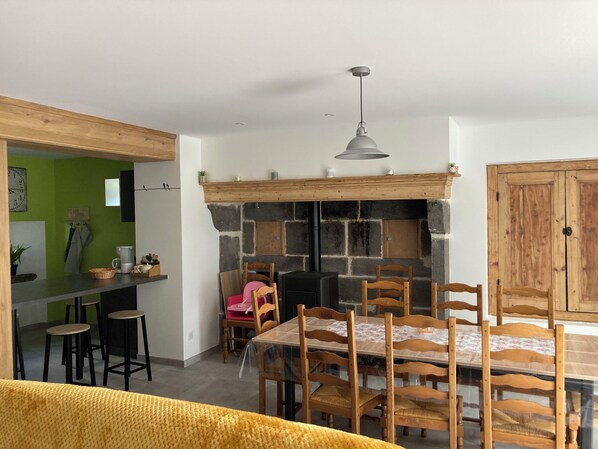 Un comedor con chimenea de piedra, sillas de madera, una mesa y una zona de bar con taburetes.