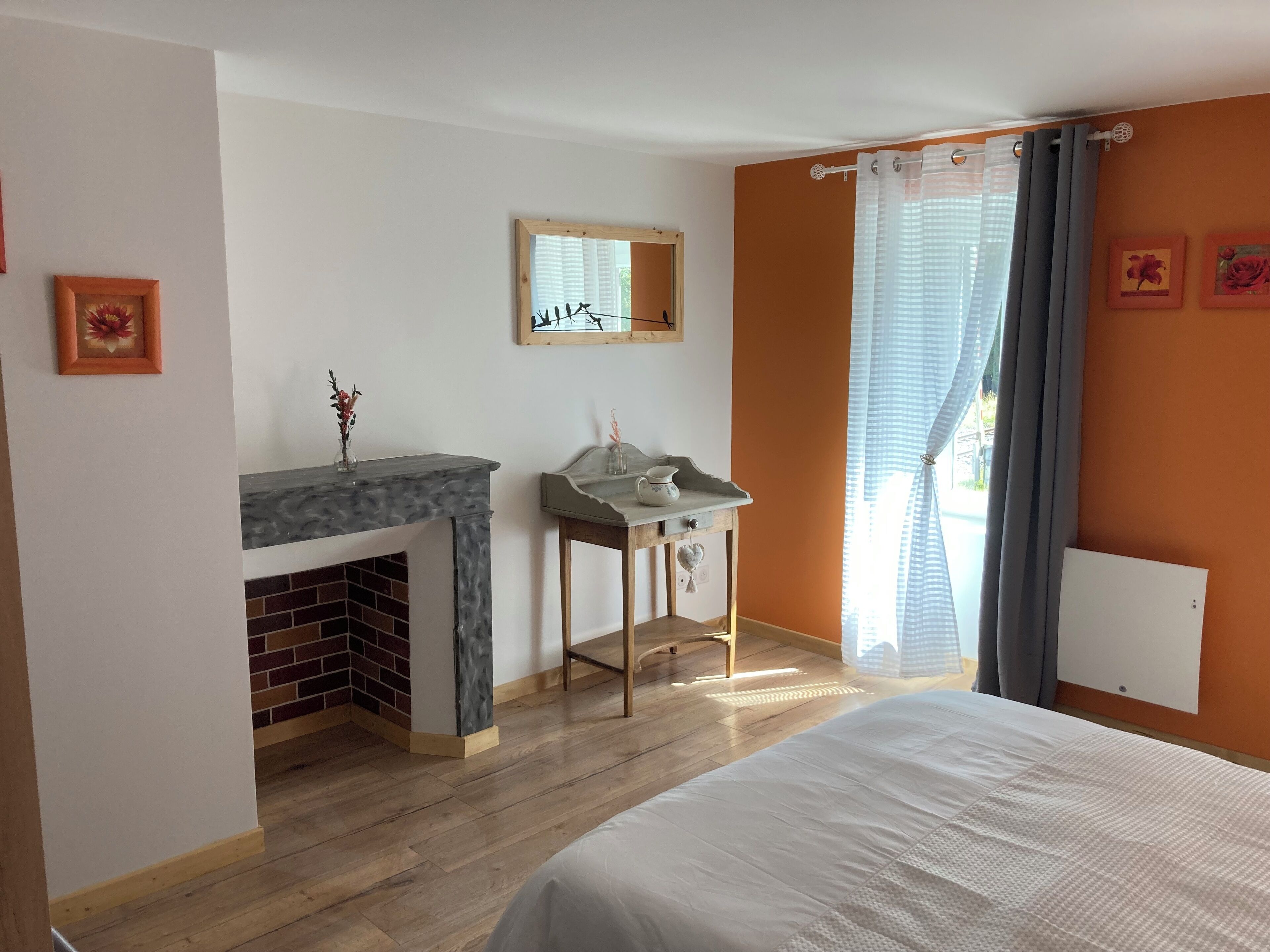 A bedroom with a bed, a fireplace, a small table with a vase, and a window with curtains.