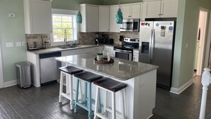 A modern kitchen with white cabinets, a granite countertop, stainless steel appliances, and a central island with bar stools.