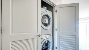 A laundry room with two stacked front-loading washing machines and a closed door. - Ayasha River-view King Bed Suite in Keystone/Broad-Ripple/Carmel (Indianapolis)