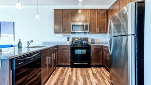 A modern kitchen with wooden cabinets, stainless steel appliances, and a granite countertop. - Ayasha River-view King Bed Suite in Keystone/Broad-Ripple/Carmel (Indianapolis)