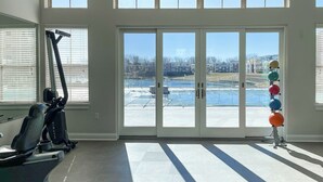 A gym with exercise equipment, large windows, and a view of a building complex. - Ayasha River-view King Bed Suite in Keystone/Broad-Ripple/Carmel (Indianapolis)