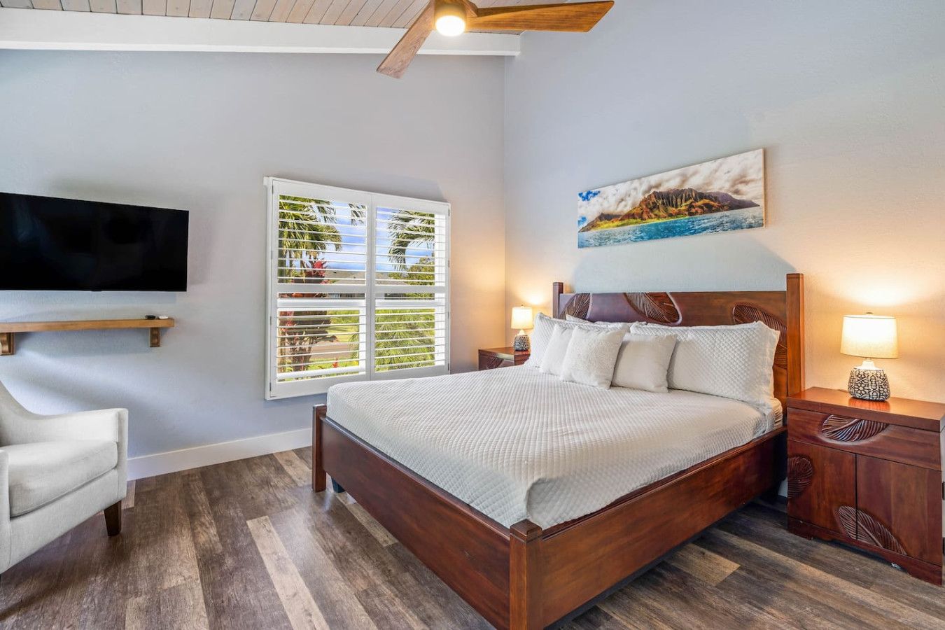 A bedroom with a large bed, a TV mounted on the wall, a window with blinds, and a painting above the bed.
