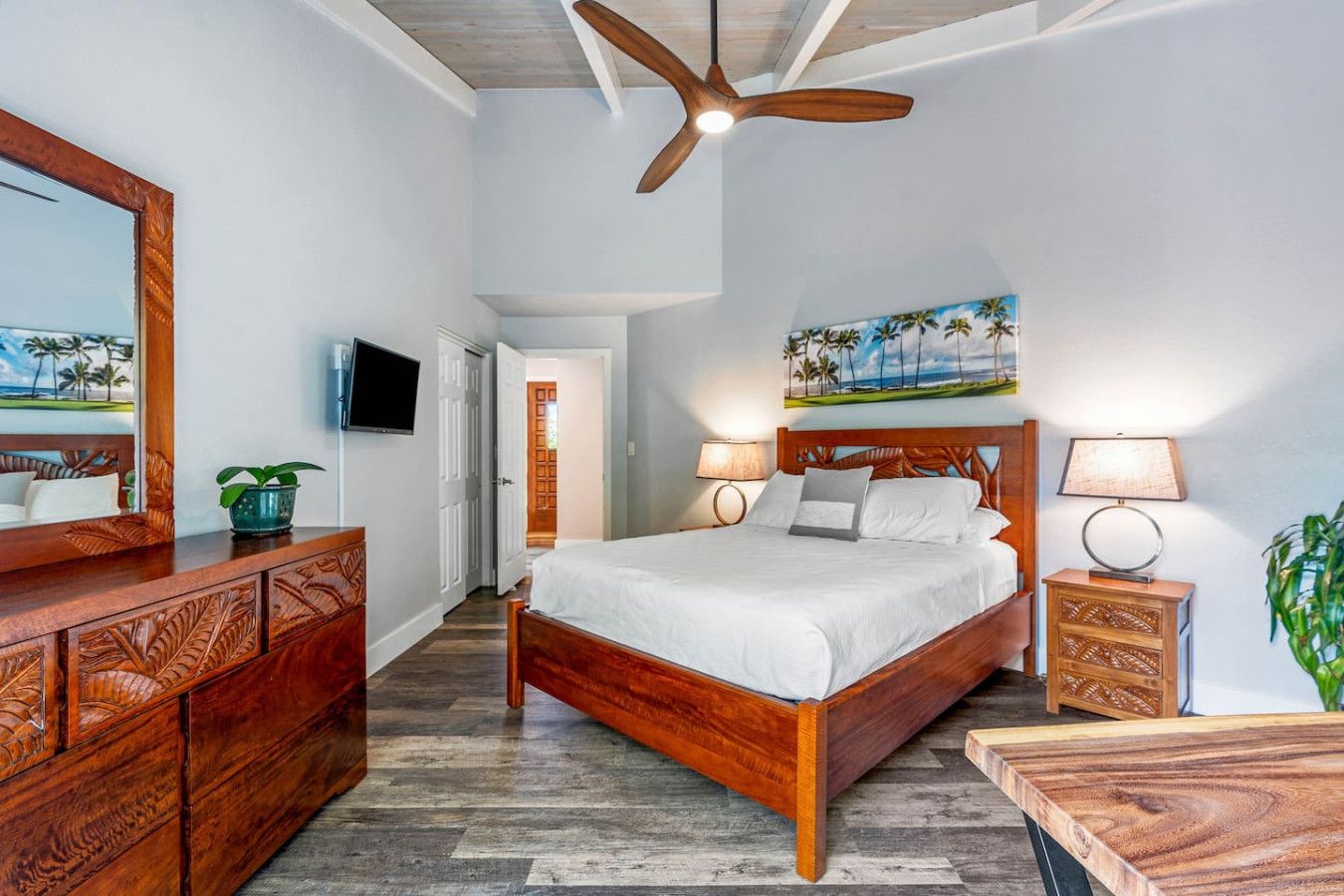 Hotelkamer met een houten bed, een plafondventilator, een televisie en een schilderij van een strand.