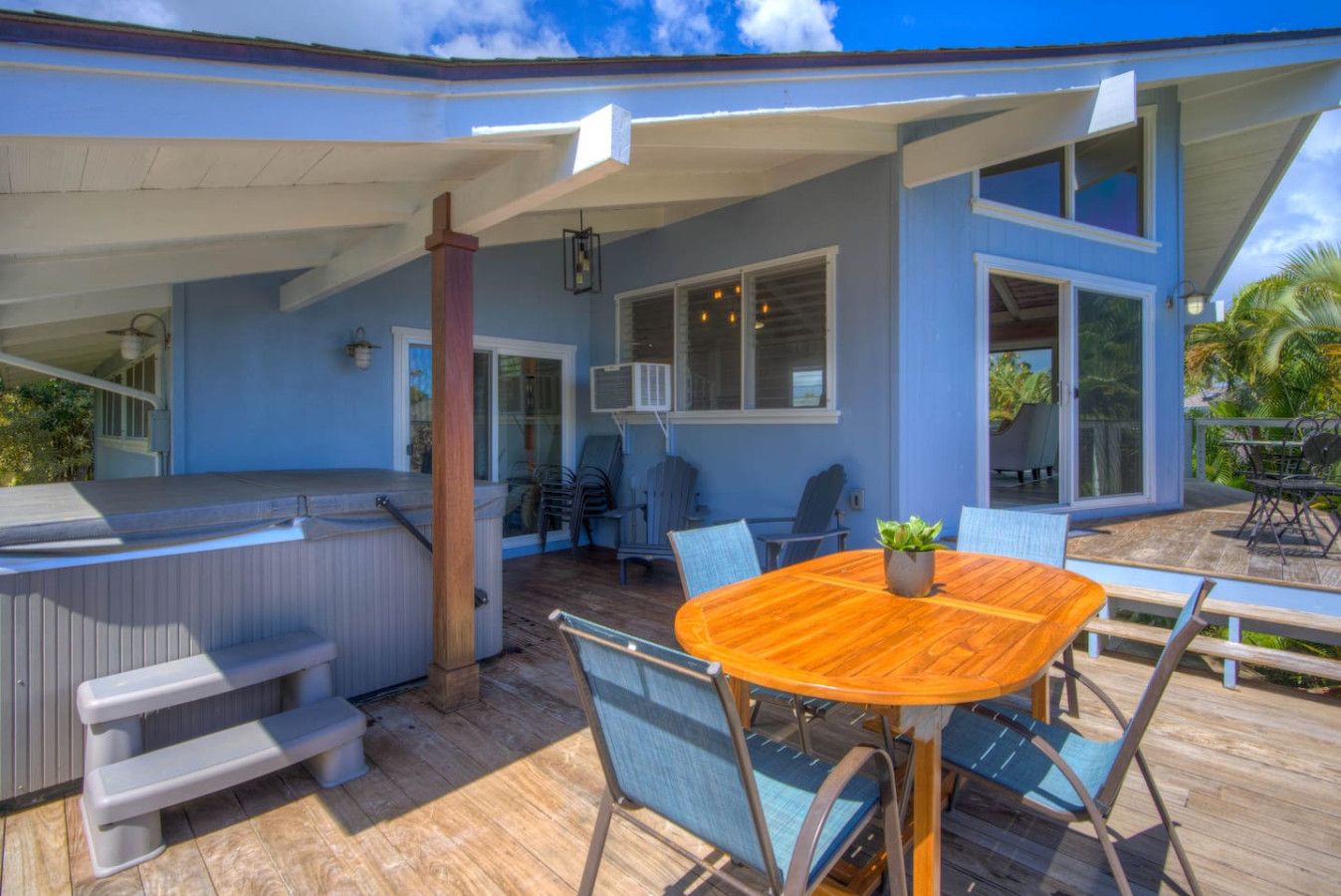A covered outdoor area with a wooden table and chairs, a hot tub, and a seating area with a view of the house.