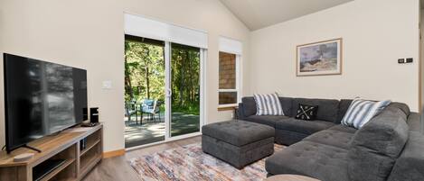 Ein modernes Wohnzimmer mit Flachbildfernseher, grauem Ecksofa und einem Holztisch.