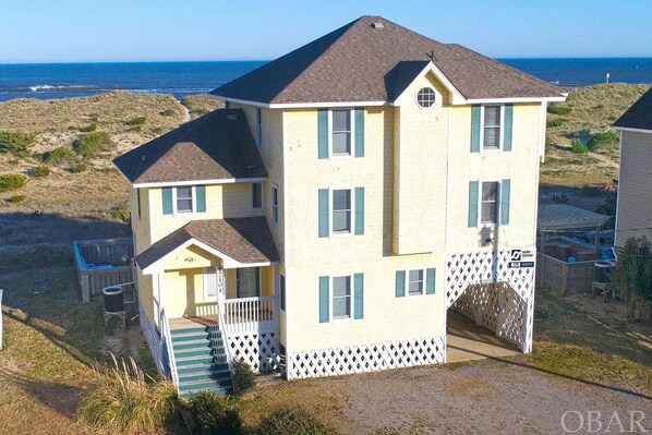 A two-story building with a balcony and a small porch, situated on a grassy area with a view of the ocean.