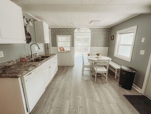 Una cocina con armarios blancos, encimera de granito, un lavabo y un comedor con mesa y sillas.