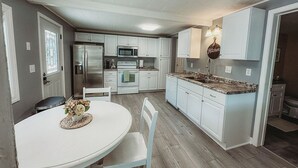 A kitchen with white cabinets, a granite countertop, and a dining area with a white table and chairs. - The Bungalow on Lake Drive (Shawano)