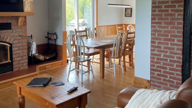 A spacious living room with a fireplace, a dining area with wooden chairs, a leather sofa, and a staircase leading to an upper level.