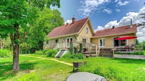 A two-story stone house with a red roof, a covered patio, and a small garden.