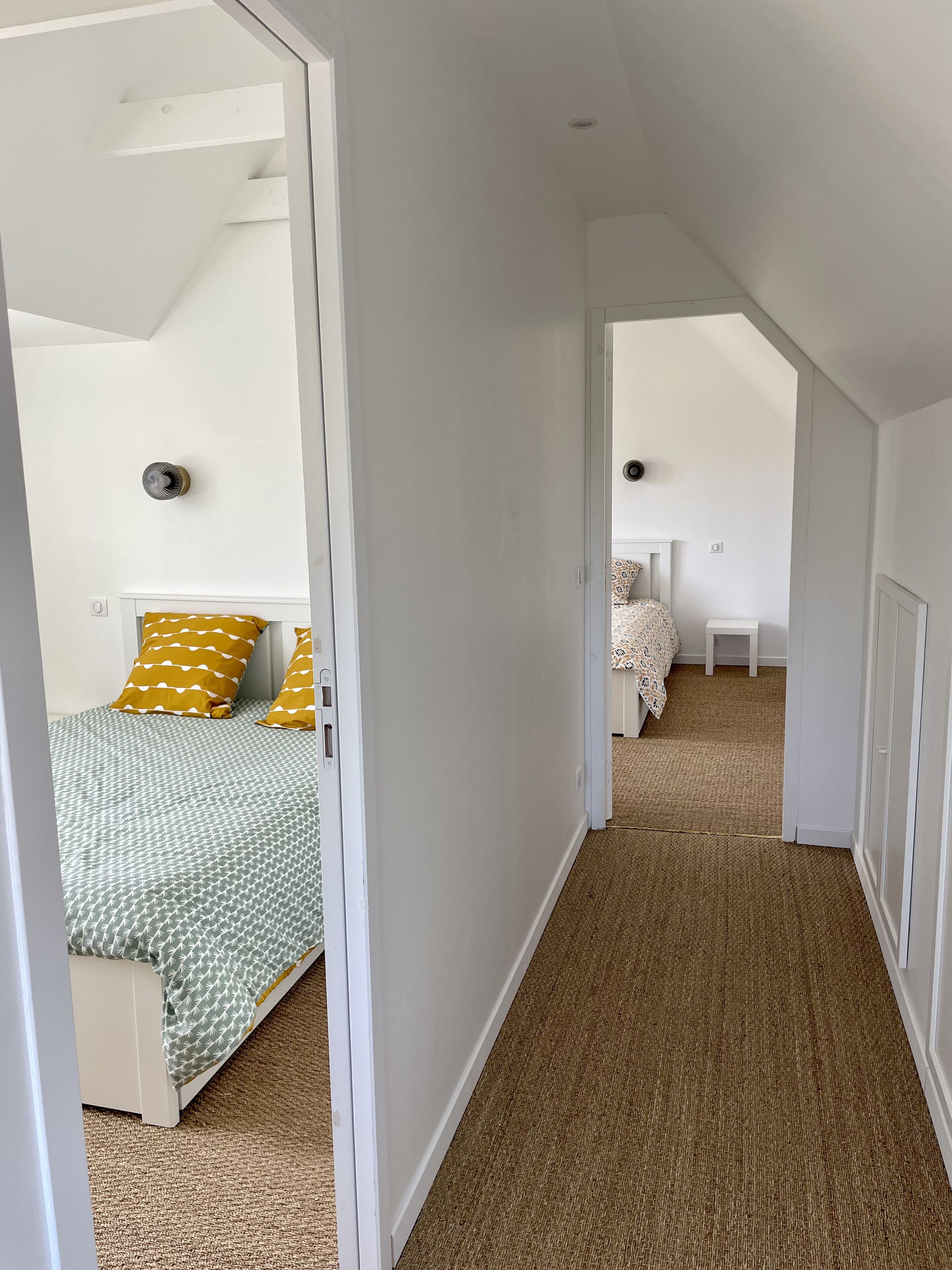 Een smalle gang met tapijtvloeren die leidt naar een slaapkamer met een bed en nachtkastje.