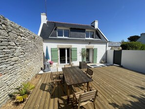 Une maison avec un mur en pierre, une terrasse en bois et un patio équipé d’une table et de chaises.