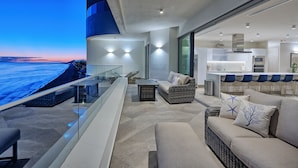 A modern outdoor living area with a glass balustrade overlooking a body of water, furnished with a sofa, chairs, and a dining table. - LUXURY NEW OCEANFRONT CONDO- Las Palomas PH 3, 5BR/BA, 4485 Total SF , Sleeps 12 (Puerto Peñasco)