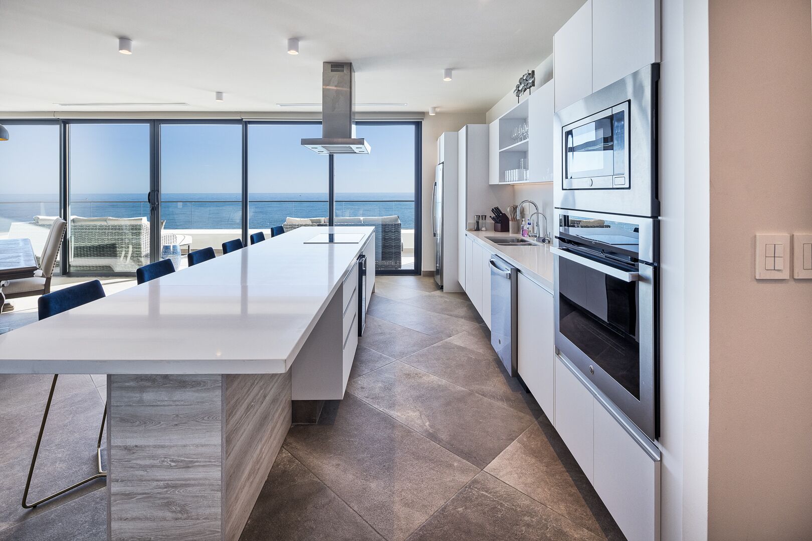 A modern kitchen with a large island, stainless steel appliances, and a view of the ocean.