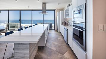 A modern kitchen with a large island, stainless steel appliances, and a view of the ocean.